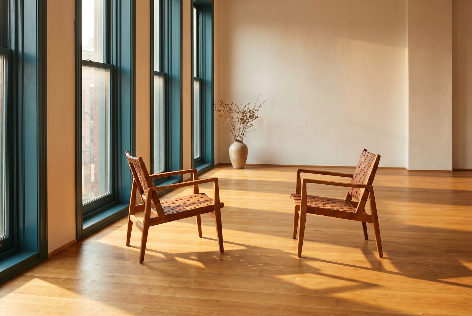 Two empty wooden chairs facing each other in a sunlit room with deep teal window frames.